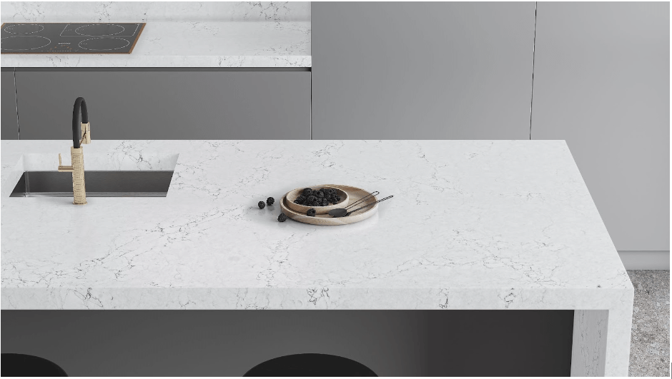 A kitchen close up shows a veined white waterfall kitchen countertop over grey cabinetry.